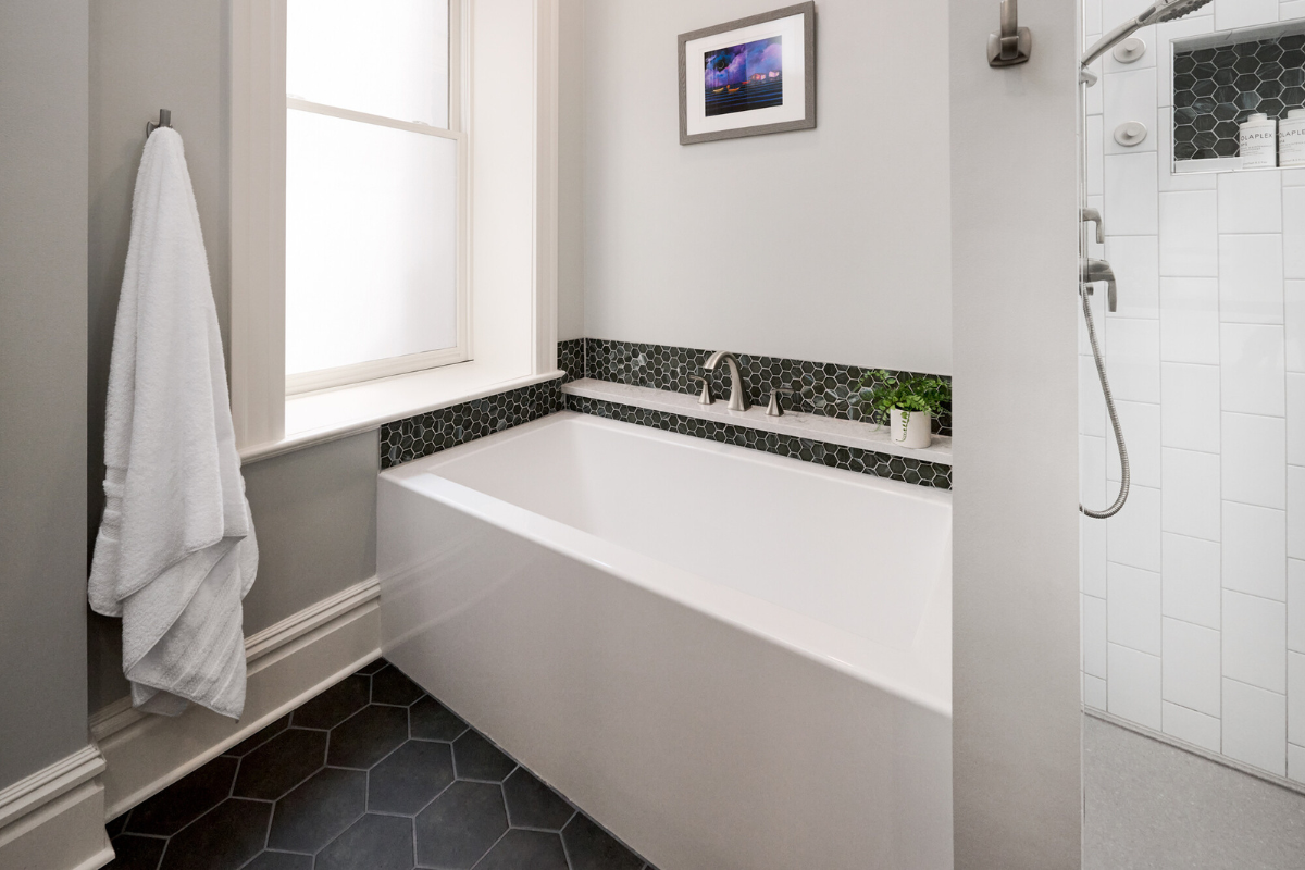 Modern bathroom featuring a freestanding bathtub, hexagonal tile accents, sleek fixtures, and a window with natural light, showcasing J.T. McDermott Remodeling Contractors' bathroom renovation expertise.