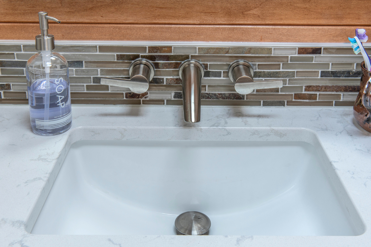 Modern bathroom sink with brushed nickel faucets, glass soap dispenser labeled 'SOAP', and decorative tile backsplash, showcasing J.T. McDermott Remodeling's expertise in bathroom renovations.