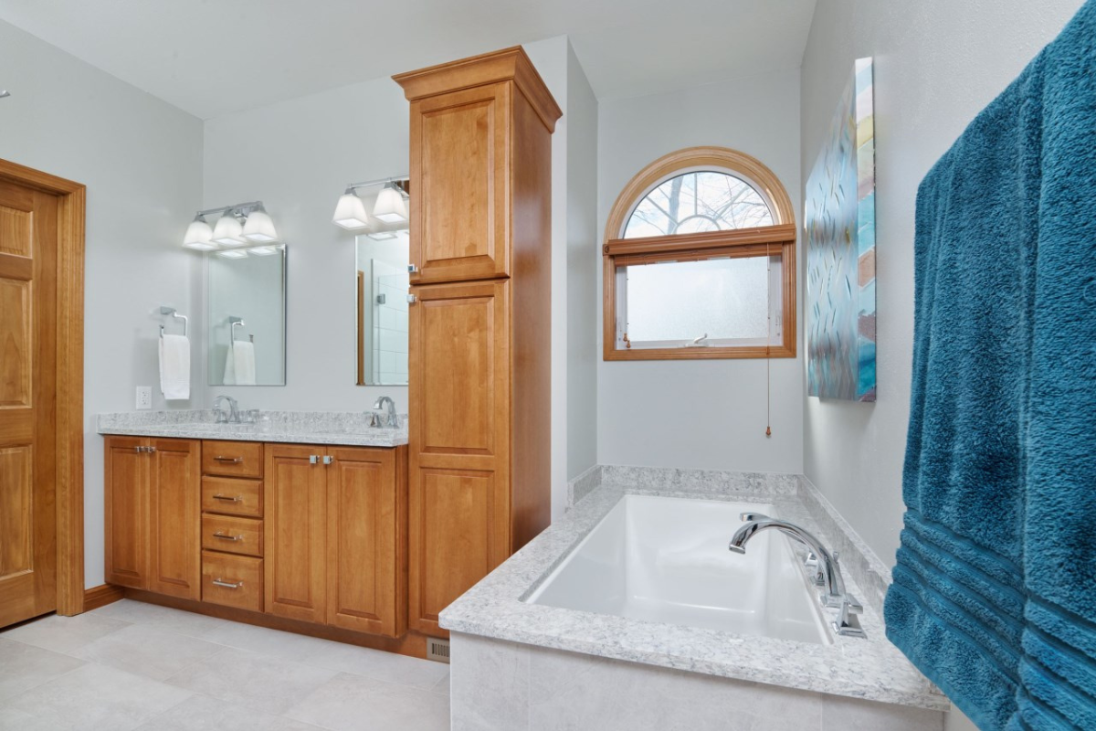Modern bathroom featuring wooden cabinetry, double sink vanity with granite countertop, a soaking tub, and a frosted window, showcasing J.T. McDermott Remodeling's expertise in bathroom renovations.