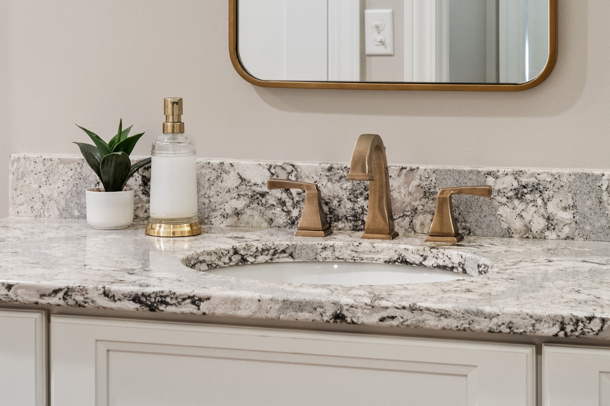 Bathroom vanity with modern bronze faucets, granite countertop, a potted plant, and a glass soap dispenser, showcasing J.T. McDermott Remodeling's design expertise.