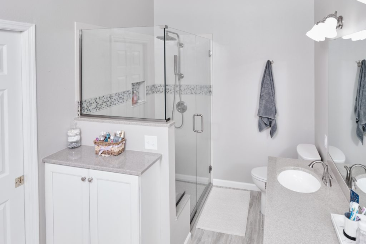 Modern bathroom featuring a glass shower enclosure, gray countertops, white cabinetry, and stylish fixtures, showcasing J.T. McDermott Remodeling Contractors' expertise in bathroom renovations.