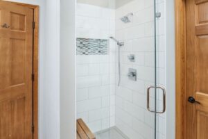Walk-in shower remodel with glass door, white tiled walls, and wood accent bench